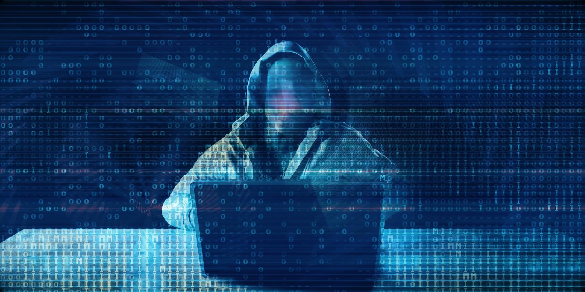A hooded figure sits in front of a laptop, surrounded by a digital backdrop of binary code, representing the theme of cybersecurity and the importance of DNS monitoring to protect against potential threats.