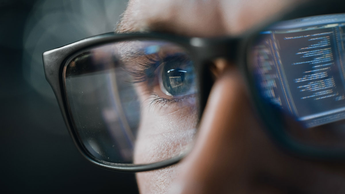 eye-close-up-glasses-observing-a-monitor-2 Close-up of a person's eye wearing glasses, focusing on a computer screen displaying code, highlighting the importance of DNS security, monitoring, and surveillance to prevent DNS infringement.